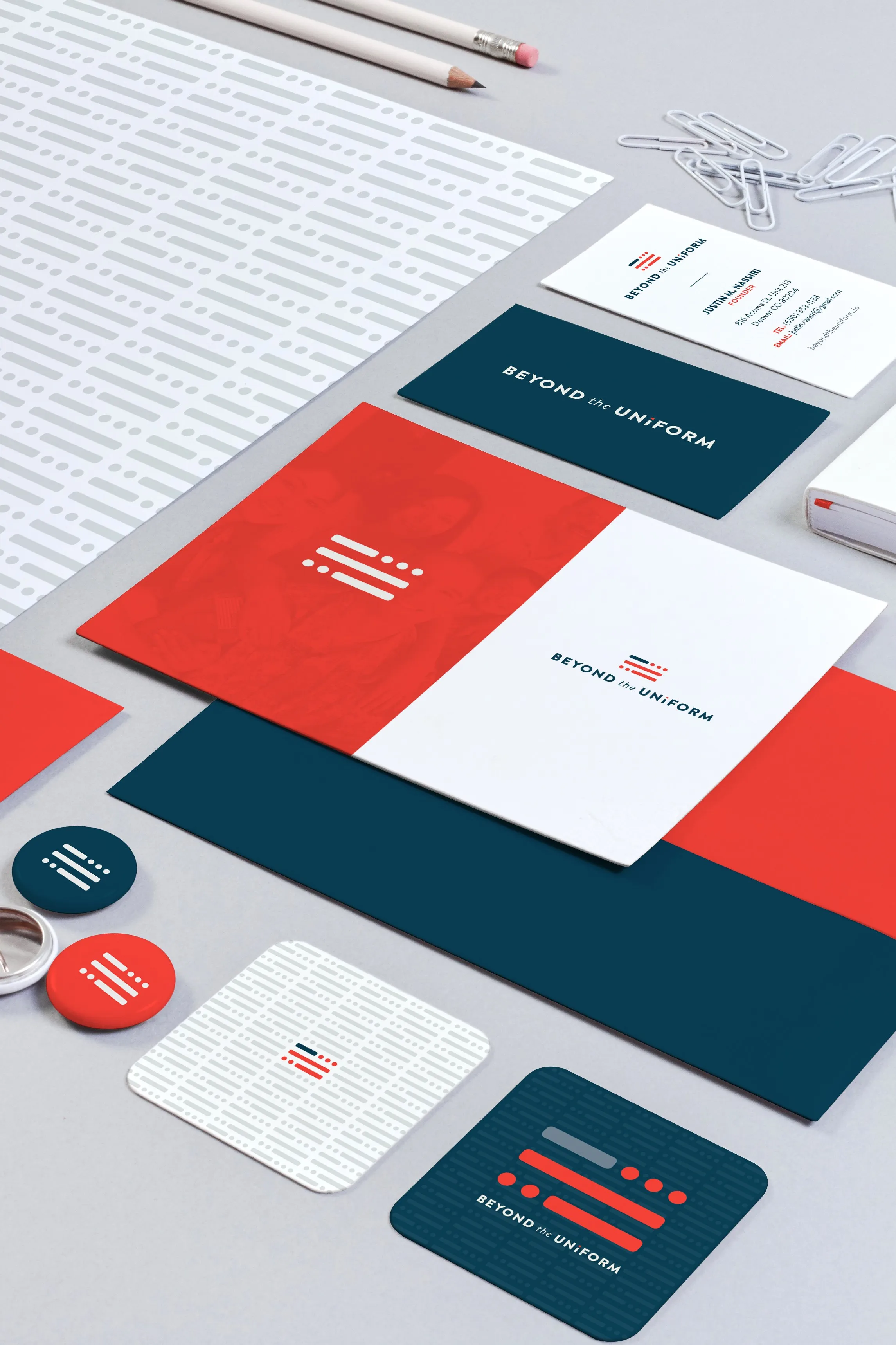 The stationery at an angle: letterhead, envelopes, business cards, buttons and a coaster in navy, warm red and white
