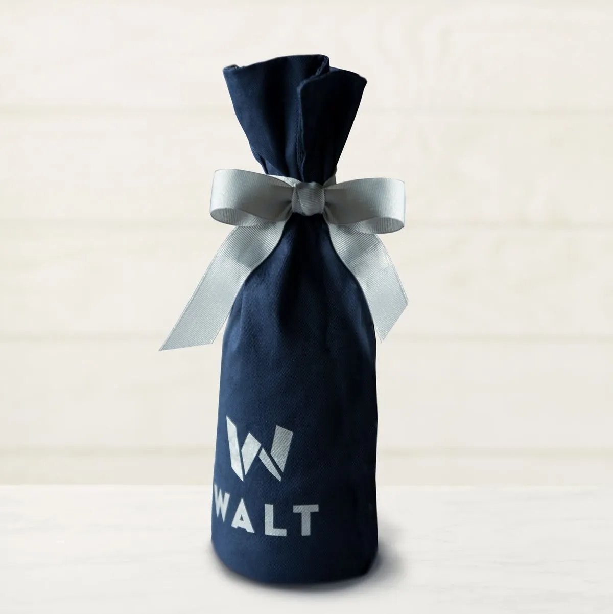 A navy cloth bottle bag tied with a silver ribbon, the W printed on the front
