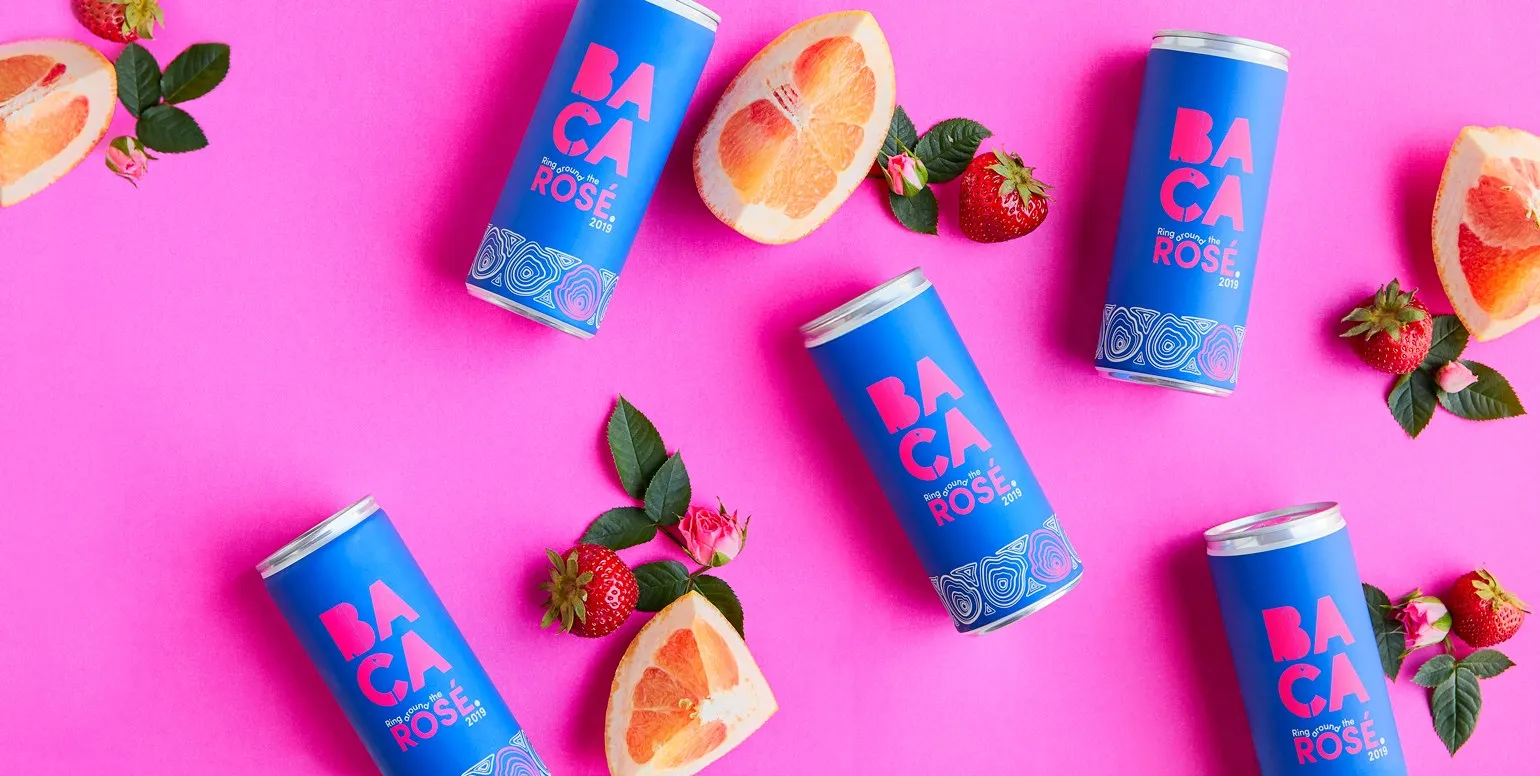 Cans of BACA Rosé scattered on hot pink with strawberries and grapefruit