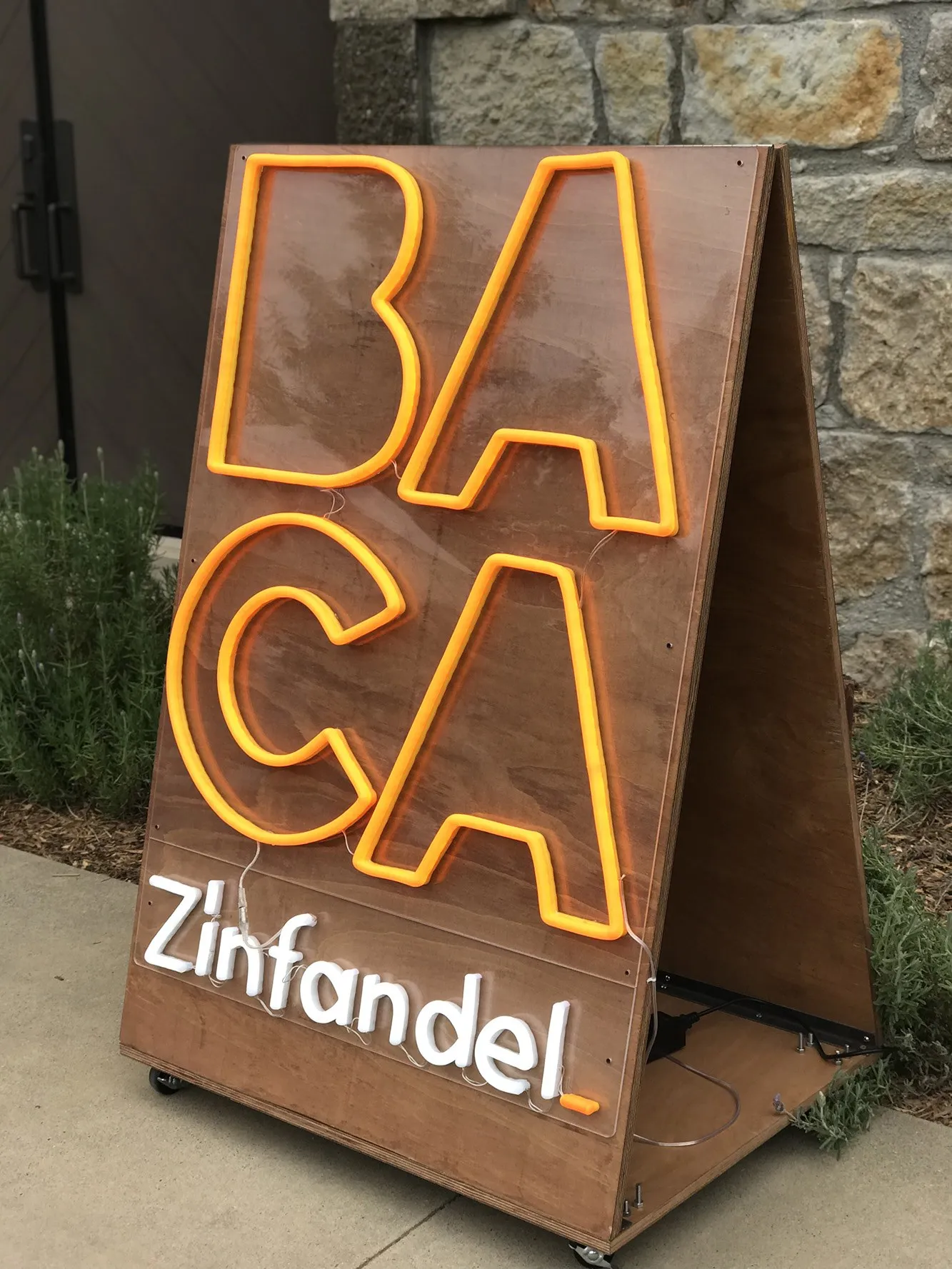 A rusted steel BACA Zinfandel sign against a stone wall